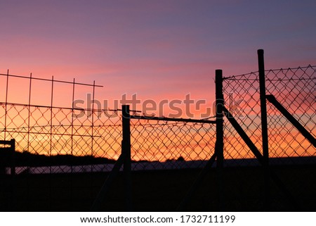 Colorful sunset behind a silouette of an wire fance