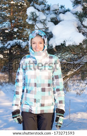 young happy woman in blue sporty checkered jacket walking in winter forest