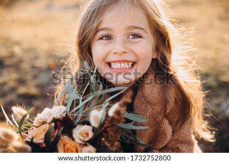 Portrait of a small stylish beautiful model girl who stands in the autumn mountains at sunset and holds a bouquet of flowers in her hands