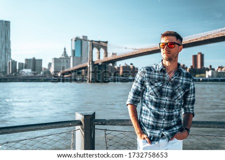 Young man standing by the Hudson river with a Brooklyn bridge in the background.