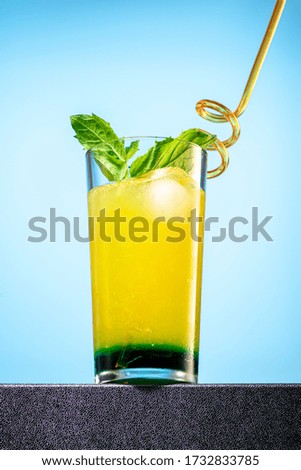 cocktail of orange juice, mint syrup and ice in a direct glass on a blue background