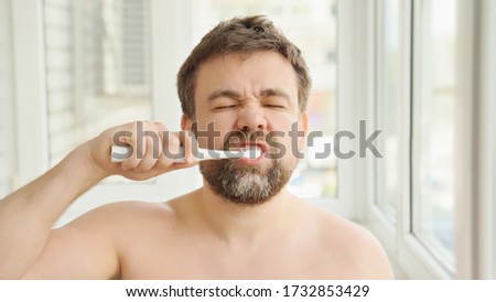 sleepy man with a beard in the morning cleans the teeth electric toothbrush. the concept of daily care and hygiene of the oral cavity. prevention of dental caries.