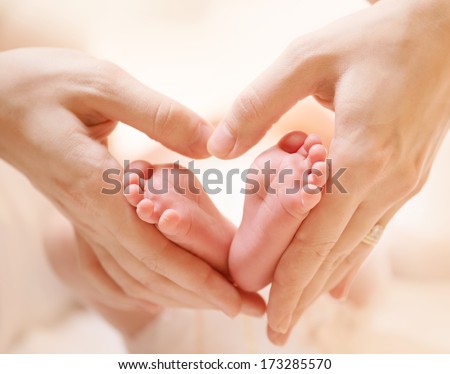 Baby feet in mother hands. Tiny Newborn Baby's feet on female Heart Shaped hands closeup. Mom and her Child. Happy Family concept. Beautiful conceptual image of Maternity 