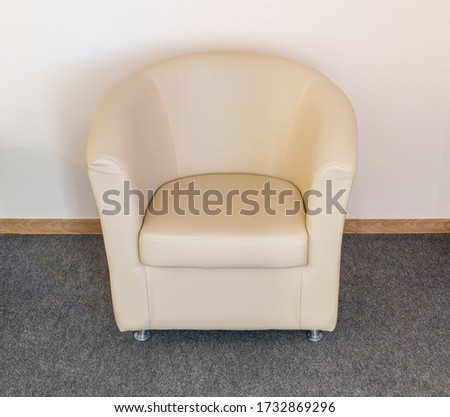 Empty armchair in style minimalism upholstered in beige artificial leather stand on fitted carpet near wall