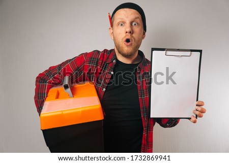 Portrait of a surprised male builder holding a bag with a tool and white paper for the text. The concept of store advertising