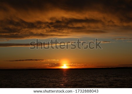 A fire is burning in the sky at sunset with lush illuminated orange clouds covering half of the clear horizon.The last glimmer near the lake.A striking contrast picture at the end of the day.Russia