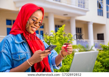 beautiful african lady sitting outside with her laptop and phone making a payment online holding her credit card