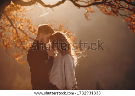 Stylish young couple in the autumn mountains. A guy and a girl hug together under a large old tree on a background of a forest and mountain peaks at sunset. Royalty-Free Stock Photo #1732931333