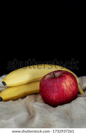 Still life photography of fruits: Apple and bananas on a cloth with black background.