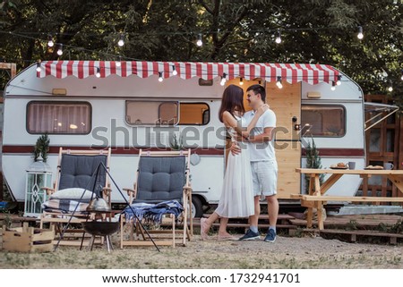 A young couple cuddles on the background of their trailer. Lovers rest outside the city, laugh, celebrate their honeymoon. Selective and Back front Focus Photoshoot with some noise on photo. Travel