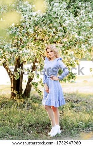 
Portrait of a young girl, blonde, European appearance in the blossom of an apple tree on nature, in spring or summer. Bright, airy photo in full growth.