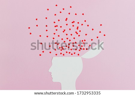 Silhouette of human's head made of white cardboard on a pink background decorated with confetti of red hearts. The concept of love. Fall in love or crazy in love. Copy space.