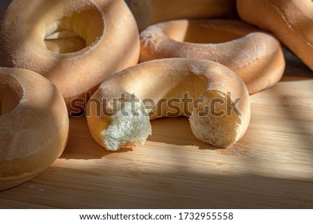 On a wooden board lie a bunch of sweet and fresh bagels. One of them is boring. Sunlight falls on the bagels.