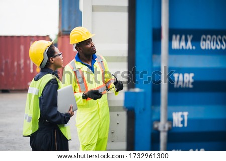 Young African american men and woman worker Check and control loading freight Containers by use computer laptop inspection at commercial shipping dock smiling felling happy. Cargo import export.