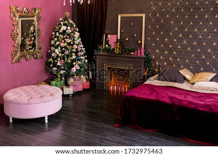 Christmas interior in purple and brown. Artificial Christmas tree with Golden and pink balloons and flowers, boxes with gifts, a fireplace with candles, a bed with a velvet blanket.