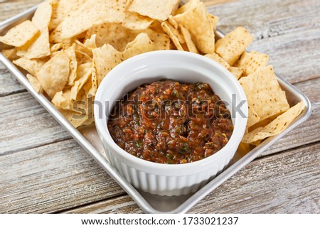 A closeup view of a metal tray of salsa with corn tortilla chips.