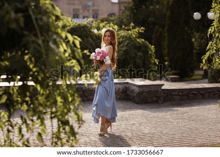 The model smiles and holds in her hands a bouquet of peonies flowers. sunset in the city for a walk. blurred background, concept
