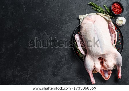 Raw whole duck, pink pepper and rosemary. Black background. Top view. Space for text
