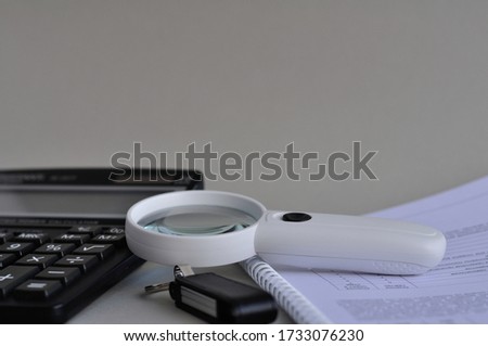 A white magnifying glass and a white pen are on the Notepad. In the background is a calculator.