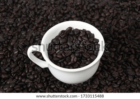 cup with roasted coffee beans inside, on the table with roasted beans top view,.