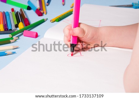 a small child draws with a pink felt-tip pen a heart in an album, copy space, top view, blue background, what to do with a quarantined child, activities for children at home
