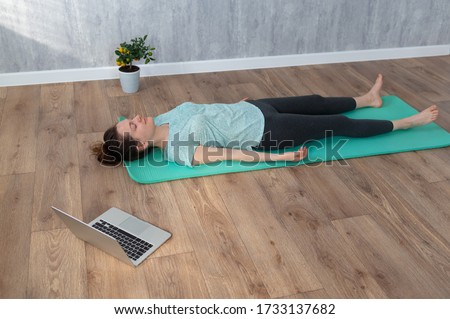 Woman in Shavasana yoga pose at home during online yoga class. Woman lying on yoga mat Royalty-Free Stock Photo #1733137682