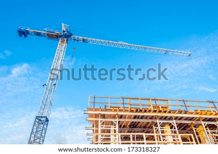 High-rise building under construction. The site with crane against blue sky with white clouds.