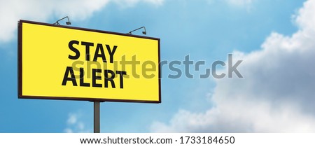 Stay Alert yellow warning sign on blue sky background. Large billboard with the slogan text. Staying alert after easing coronavirus lockdown restrictions, end of Covid-19 quarantine concept Royalty-Free Stock Photo #1733184650