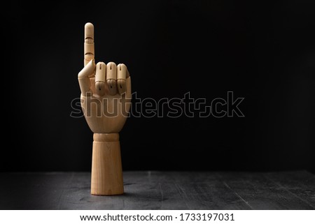 Picture of a wooden hand. It is holding index finger up to represent number one or one. It can also represent the direction guideline. The hand is placed on a wooden table on black isolated background