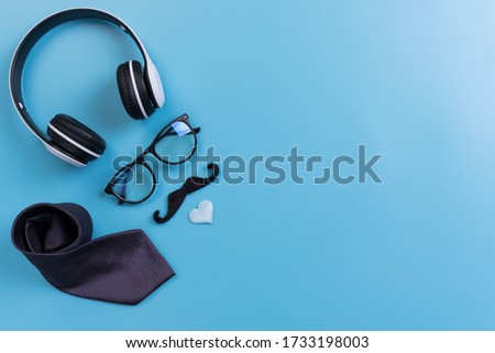 Happy Fathers Day background concept.Decorated headphone, eyeglasses,  necktie, mustache light blue heart on light blue pastel background with copy space. Top view, flat lay.