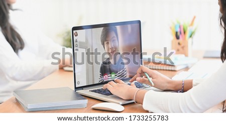 Cropped of beautiful woman hands typing on computer laptop that video calling with her boy friend while sitting at the wooden working desk over her colleague as background.