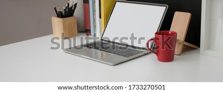 Cropped shot of stylish worktable with blank screen laptop, mug, stationery and books on white desk  
