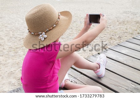 girl with cap making a selfie with mobile phone on the beach