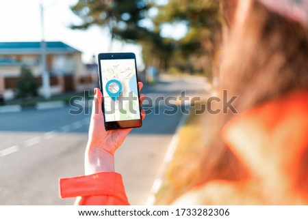 A woman's hand holds a smartphone with an online map that has a blue geolocation icon. A blurred street is visible in the background. Close up. Concept of online navigation and GPS