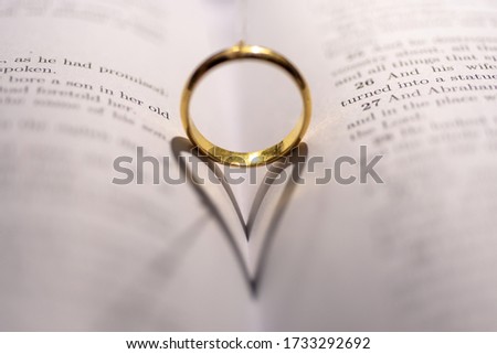 A wedding Ring on the bible with shadow of heart shape on the page