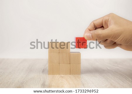 Hand picking a red cube wooden block toy stacked without graphics for Business design concept and activity for child foundation practice skills.