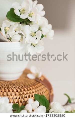 
Delicate, white flowers of an apple tree in a porcelain cup with a golden handle. The dishes are on a textured rattan bag. The concept of spring, ecology and good morning. Copy space for text.