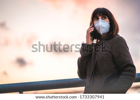 A young brunette talking on the phone with a mask on a sunset. First walks of the uncontrolled Covid-19 pandemic