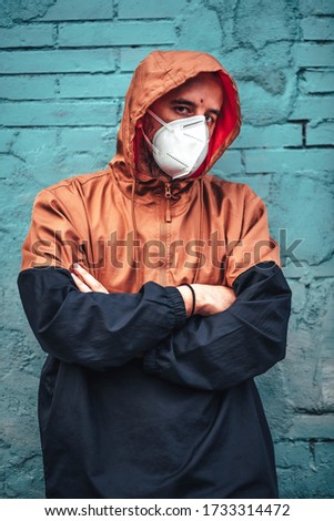 A young Caucasian man wearing a mask and leaning against a wall staring intently. First walks of the uncontrolled Covid-19 pandemic