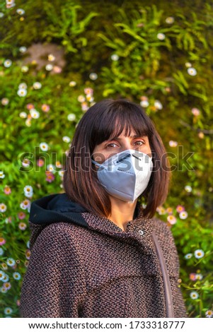 A young woman with a mask next to a beautiful daisies. First walks of the uncontrolled Covid-19 pandemic