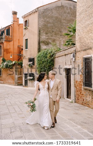 Italy wedding in Venice. The bride and groom walk along the deserted streets of the city. The newlyweds hug, dance, hold hands against the backdrop of picturesque red brick houses.