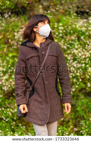 Lifestyle of a young brunette with Caucasian mask in a park with daisies in the background. First walks of the uncontrolled Covid-19 pandemic