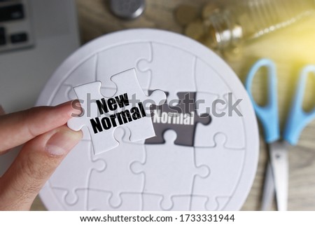 New Normal from nornal life concept. Image contain a man hand holding a piece of puzzle to put on top the old one with nice business tools in the background with beautiful flare.