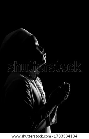 The image of an Asian Muslim boy who is praying with tranquility and faith, with the light from the studio lights from behind, with copy space.