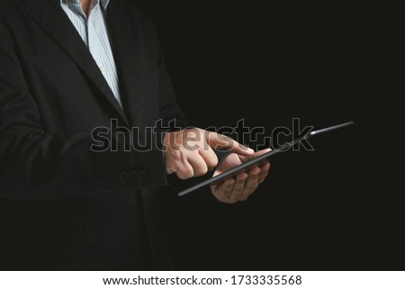 Close-up businessman wearing a black suit holding a tablet and touchscreen at monitor tablet on a black background. Concepts for business executives, financiers. Use of technology in the digital.