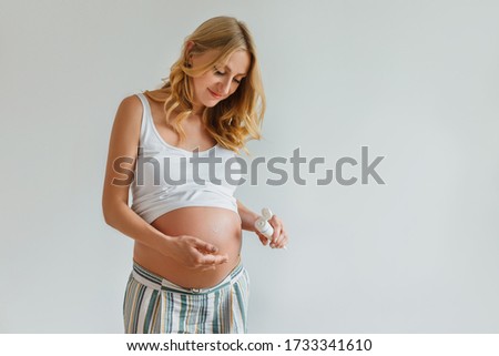 Pregnant blonde woman applying cream for belly to prevent stretch marks. Future mother holding in hands tube with lotion for skin care. Concept of health and body care, beauty during pregnancy Royalty-Free Stock Photo #1733341610