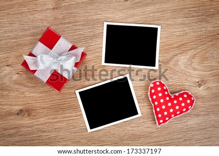 Blank photo frames and small red gift box on wooden background