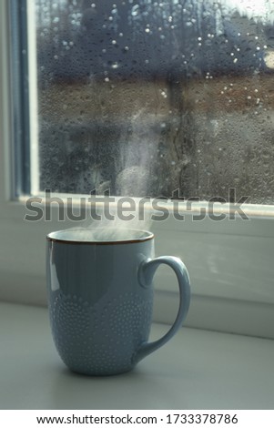 Cup of hot drink near window on rainy day