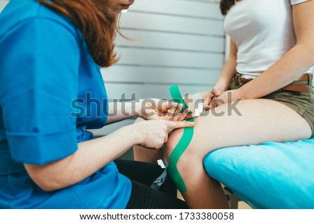 Girl physiotherapist applying kinesiotape or neuromuscular bandage to her patient in the clinic. Royalty-Free Stock Photo #1733380058
