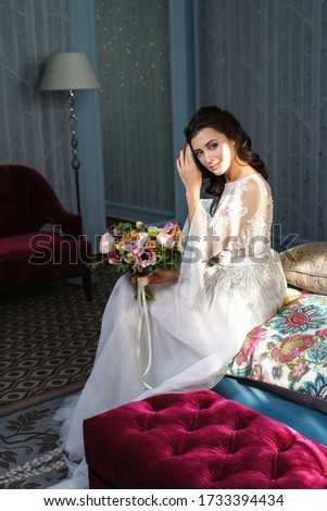 Portrait of an attractive young European Caucasian bride in a white wedding dress with a bridal bouquet in the interior of a luxury hotel. Wedding morning.
